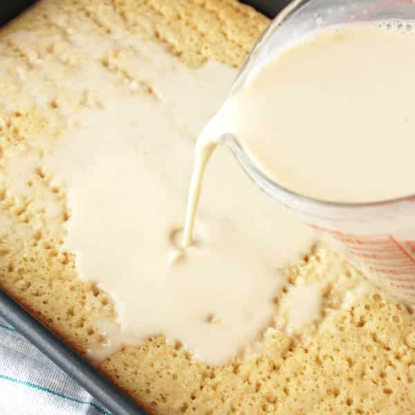 Uma forma retangular com uma massa de bolo branco cortada ao meio, cheia de furos, com uma simples calda de leite para molhar bolo.