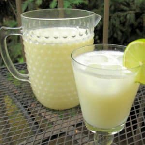 Uma jarra de vidro e um copo de vidro decorado com limonada com leite condensado, uma fatia fina de limão